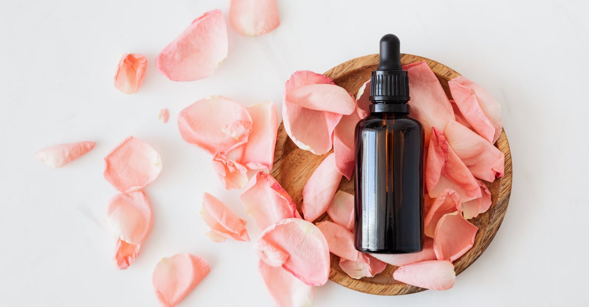 What is Essential Travel? - Top view of empty brown bottle for skin care product placed on wooden plate with fresh pink rose petals on white background isolated