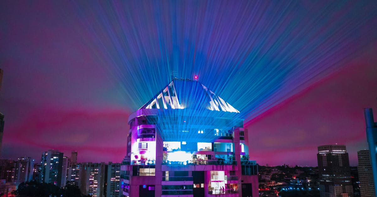 What is good accommodation for festival (camp or hostel)? - Modern building with glass roof illuminating sky with colorful lights and located in contemporary city district at night time