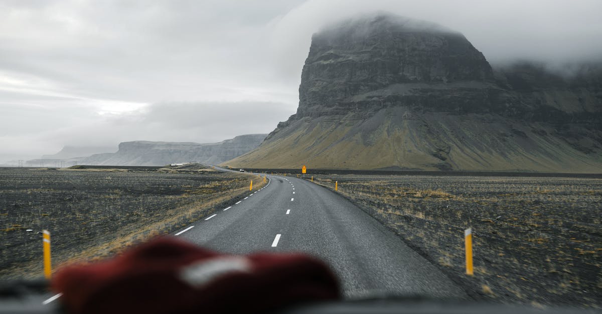 What is the best way to travel cheap through Scotland? - Through glass of empty asphalt road going through valley with mountain slopes against foggy sky