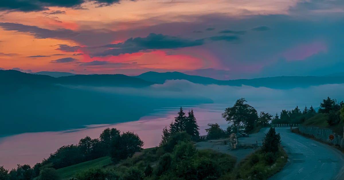 What is the best way to travel to the West Bank? - Spectacular scenery of narrow asphalt road running along tranquil river in hilly grassy terrain beneath majestic bright sunset sky