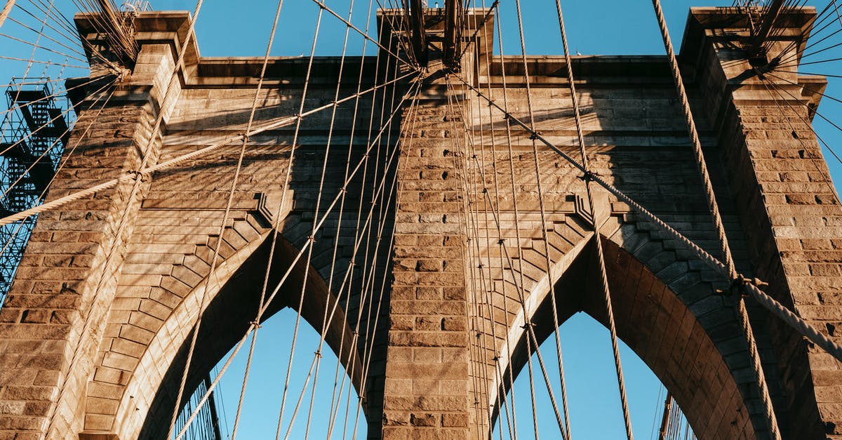 What is the cheapest way to get from South America to Australia? - Low angle of famous Brooklyn brick arches with ropes on top of bridge in metropolis