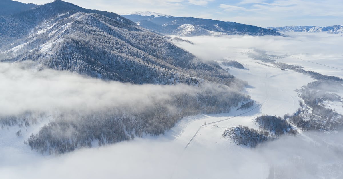 What is the cheapest way to see snow from Singapore? - Drone view of snowy valley among mountains covered coniferous forest and road going between mountain ridge through clouds in sunny winter day