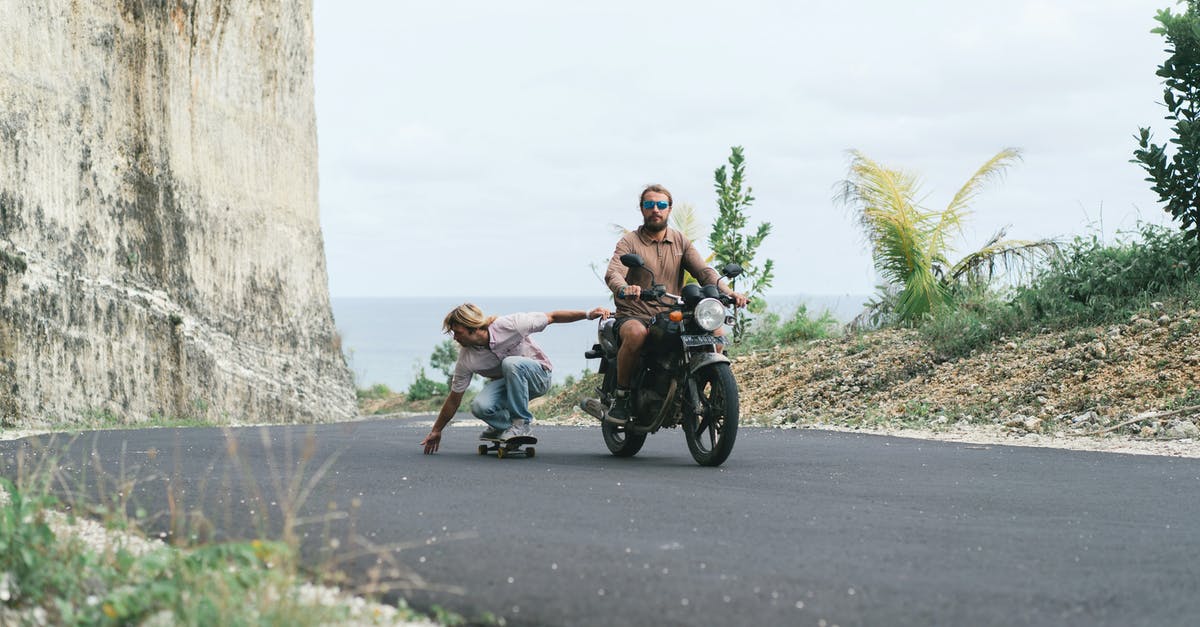 What is the experience of driving in Thailand? [closed] - Driver of motorbike riding sitting man on skateboard on road