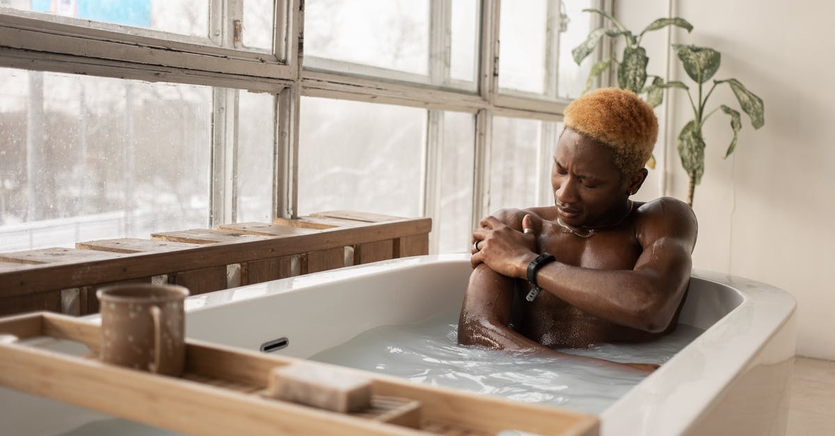 What is the red light in the hotel bath for? - Young African American man with dyed hair and accessory sitting in bathtub full of water in light room with shabby window frames