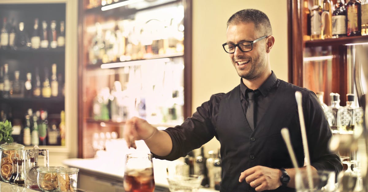 What is the tipping process in restaurants in the US? - Happy young male barkeeper standing at counter and preparing alcohol cocktail for order while working in modern pub