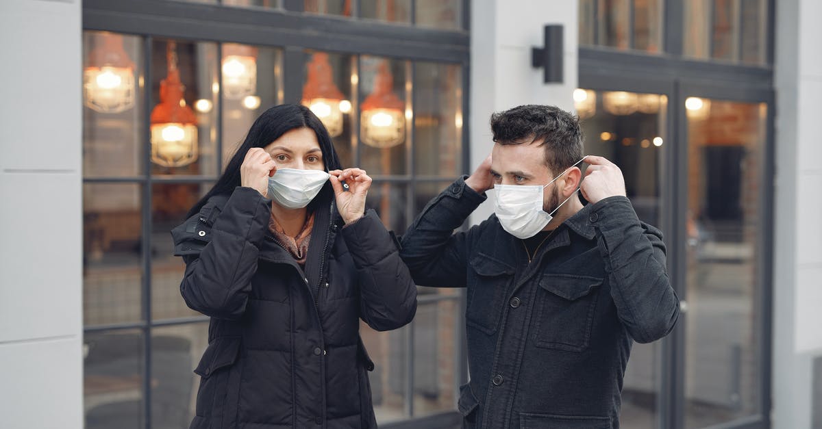 What is the typhoid fever risk for an un-vaccinated toddler in Mexico City? [closed] - Young couple adjusting medical masks against urban building exterior