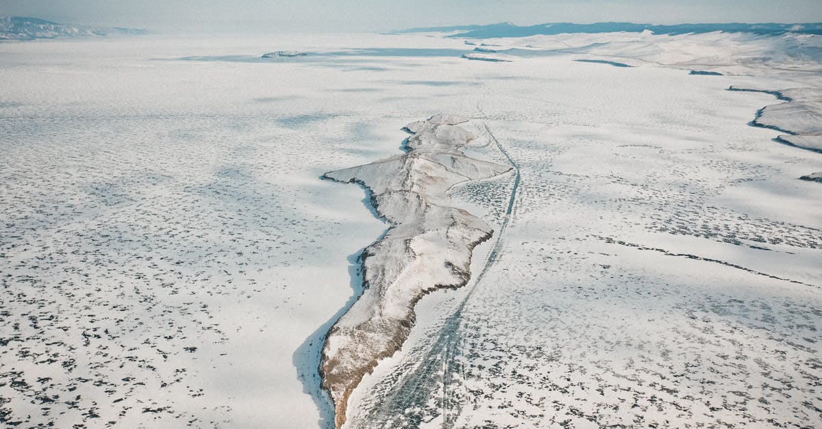 What is this formation on sea, seen from the air? - Drone view of rocky formation on icy ocean with snow under cloudy sky in wintertime