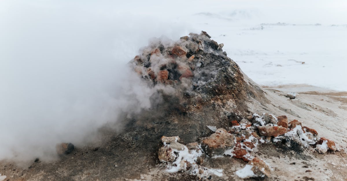 What is this formation on sea, seen from the air? - From above of small rock on dry snowy coast behind wavy ocean in fog under sky in winter