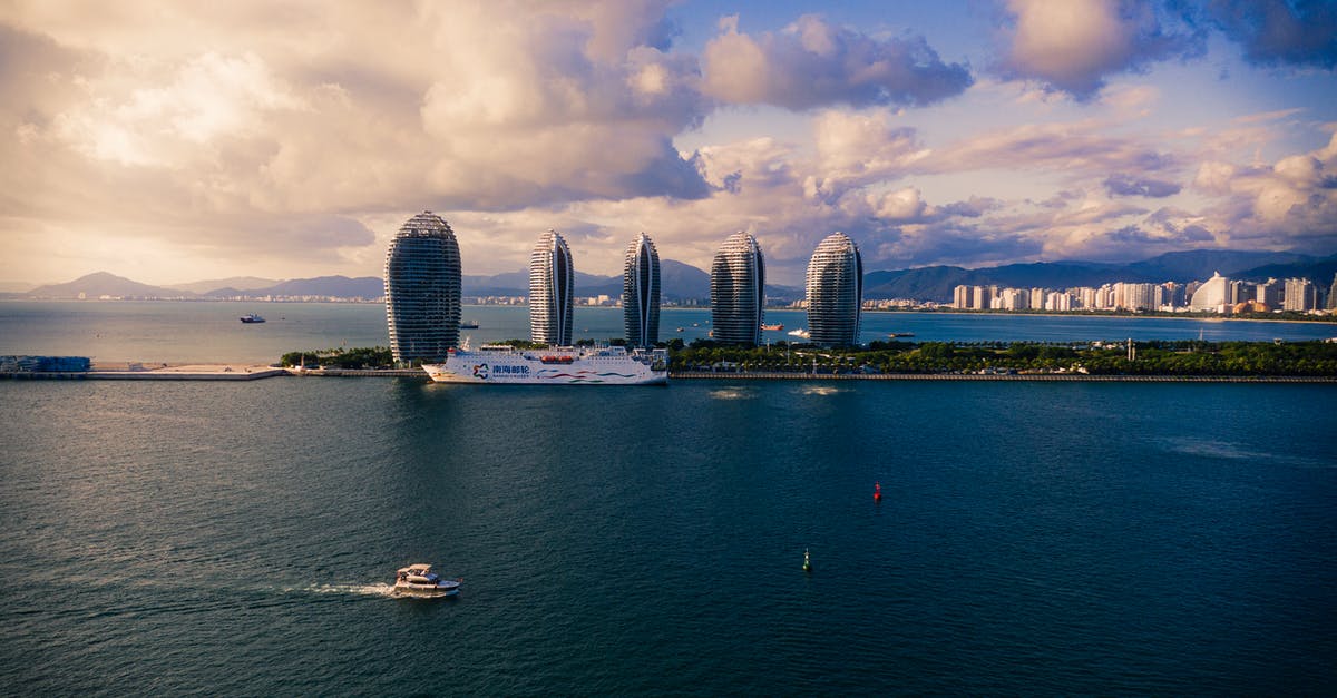 What is this island in the South China Sea called? - Modern cruise ships and boats floating on calm sea against cloudy sky near futuristic skyscrapers located on Phoenix Island in China