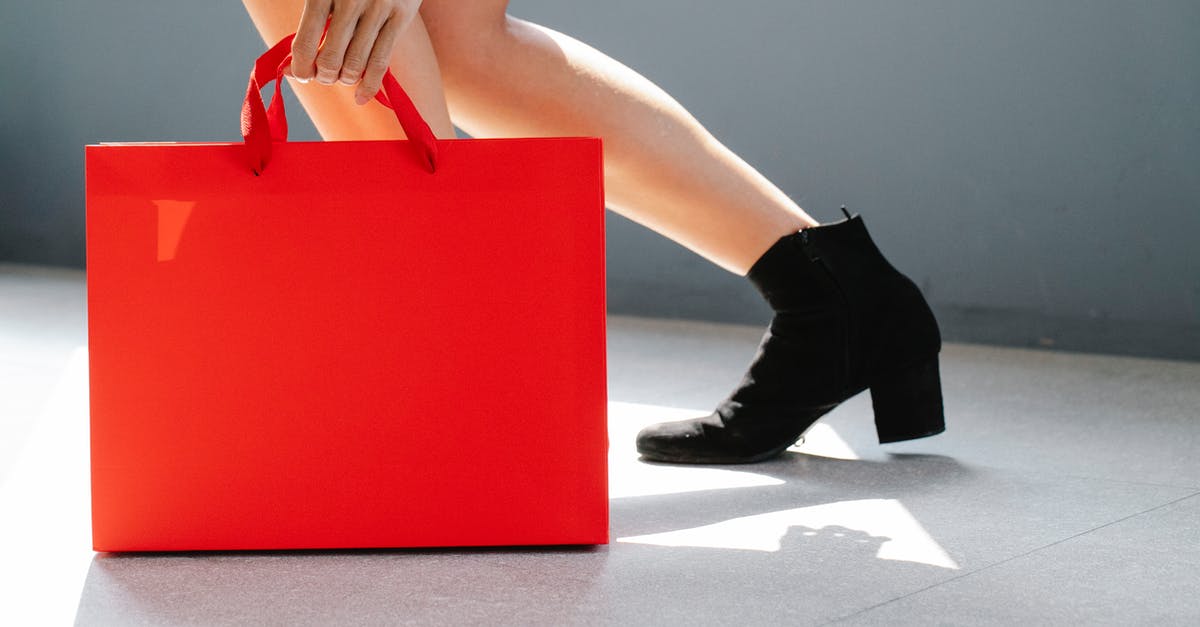 What is this "nekoya" shop advertising? - Side view of crop unrecognizable female in trendy boots holding red paper bag while standing on street on sunny day after shopping