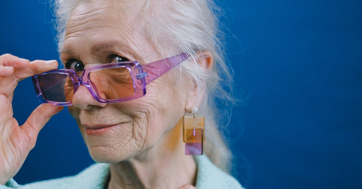 What kind of proof of residency is accepted by Disneyland? - Portrait of elegant smiling gray haired elderly female wearing purple sunglasses and earrings looking at camera against blue background