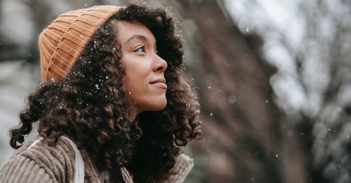 What kind of weather can I expect in Maui in October? - Side view of dreamy young black female in knitted hat looking up in town on snowy day