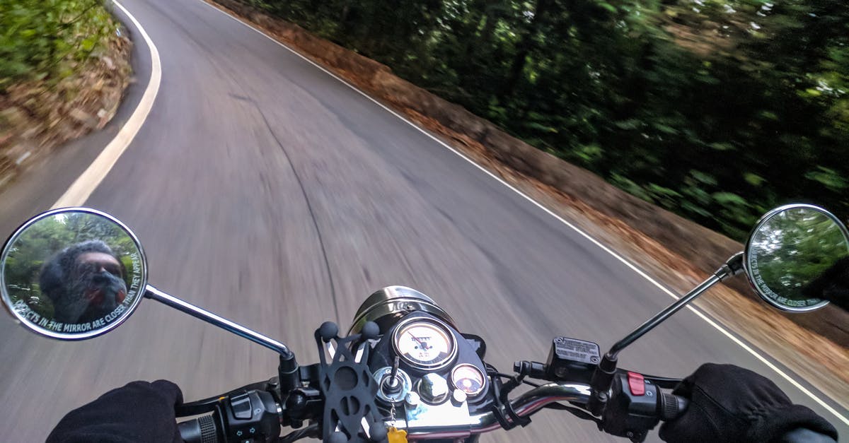 What measures can one take to keep a motorcycle safe during a road trip? - Person Driving Motorcycle on Curved Concrete Road Near Trees