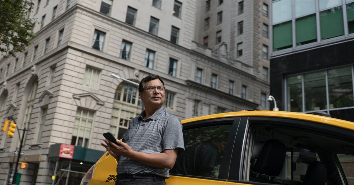 What mobile taxi app can I use in Kutaisi Georgia? - Low angle of serious ethnic male scrolling mobile phone while leaning on yellow car in downtown