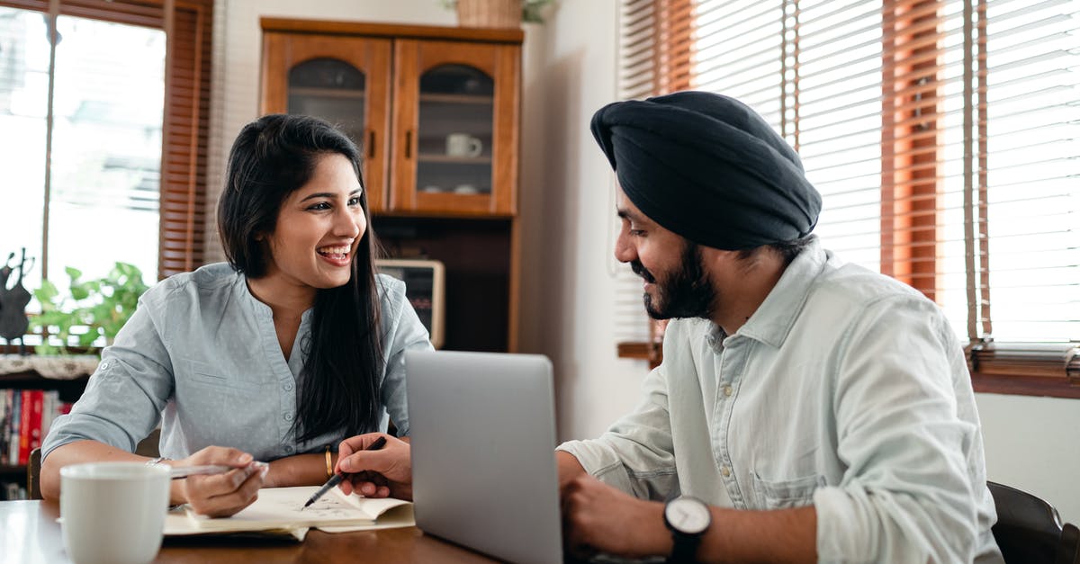 What online communities exist to help solo travellers meet up? - Laughing Indian woman with husband sitting at table and discussing project while working together with laptop and notebook at home