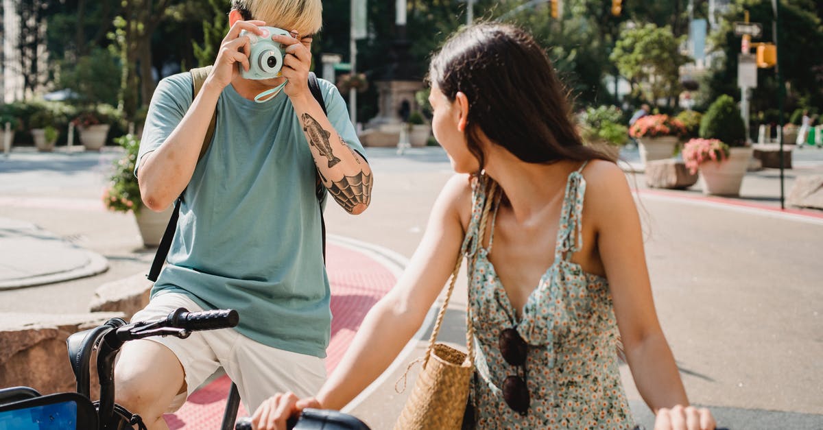 What path do flights across Australia take? - Anonymous male with instant camera taking picture of unrecognizable girlfriend on bicycle while standing on pavement on street in city