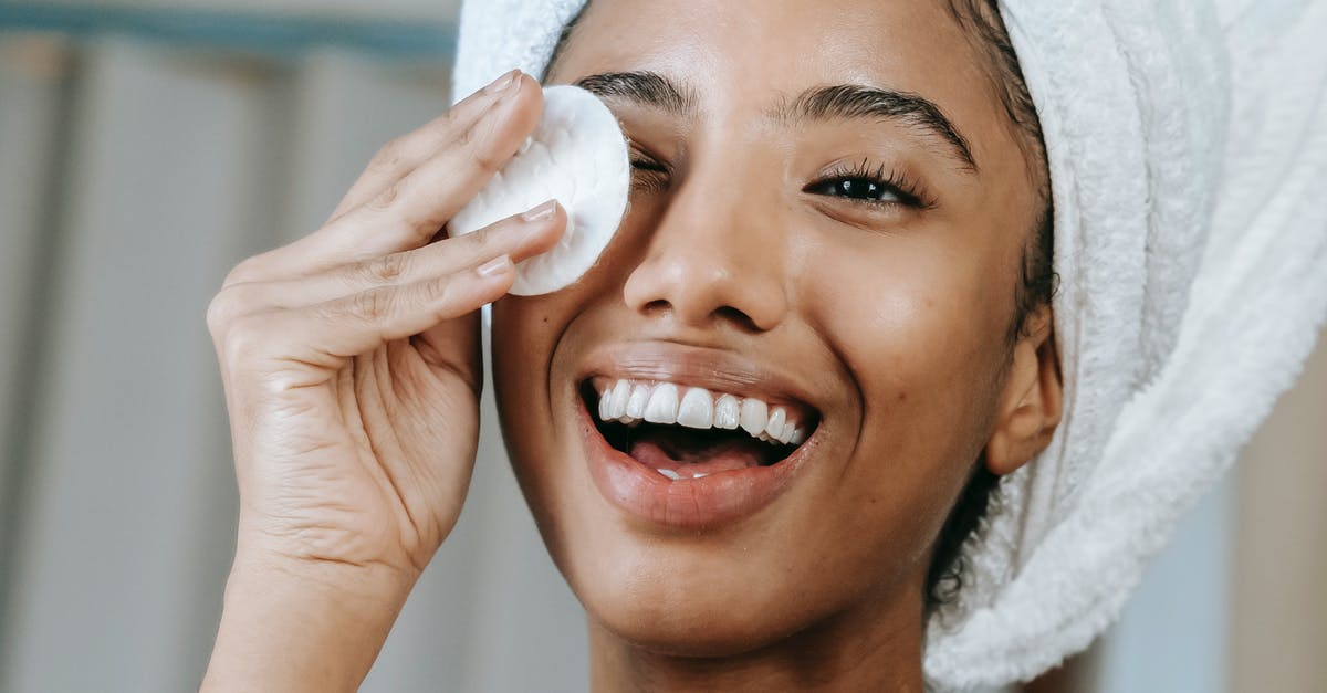 What restrictions apply to layovers in the Schengen area? - Cheerful ethnic female wrapped in towel turban moisturizing face with lotion while smiling happily