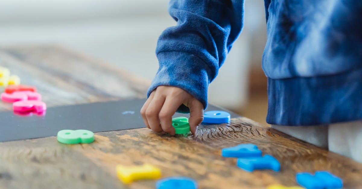 What should I think of and prepare when flying with kids? - Crop anonymous ethnic boy taking plastic number from wooden table while learning math