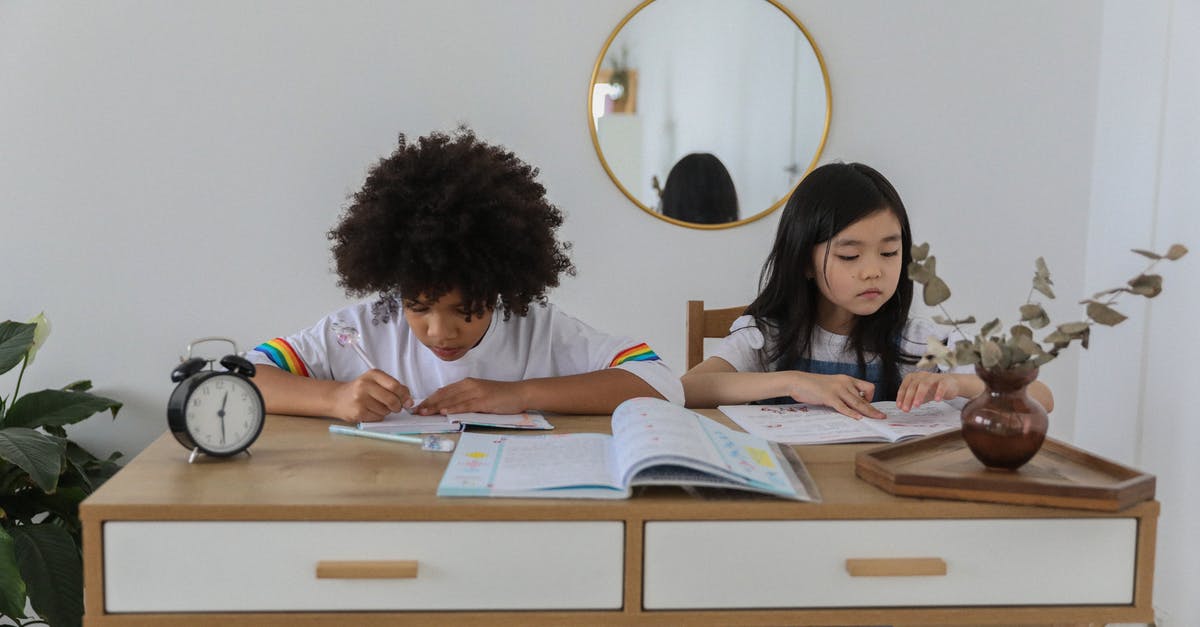 What should I think of and prepare when flying with kids? - Concentrated multiracial girls sitting at table with notebooks and doing homework in cozy room