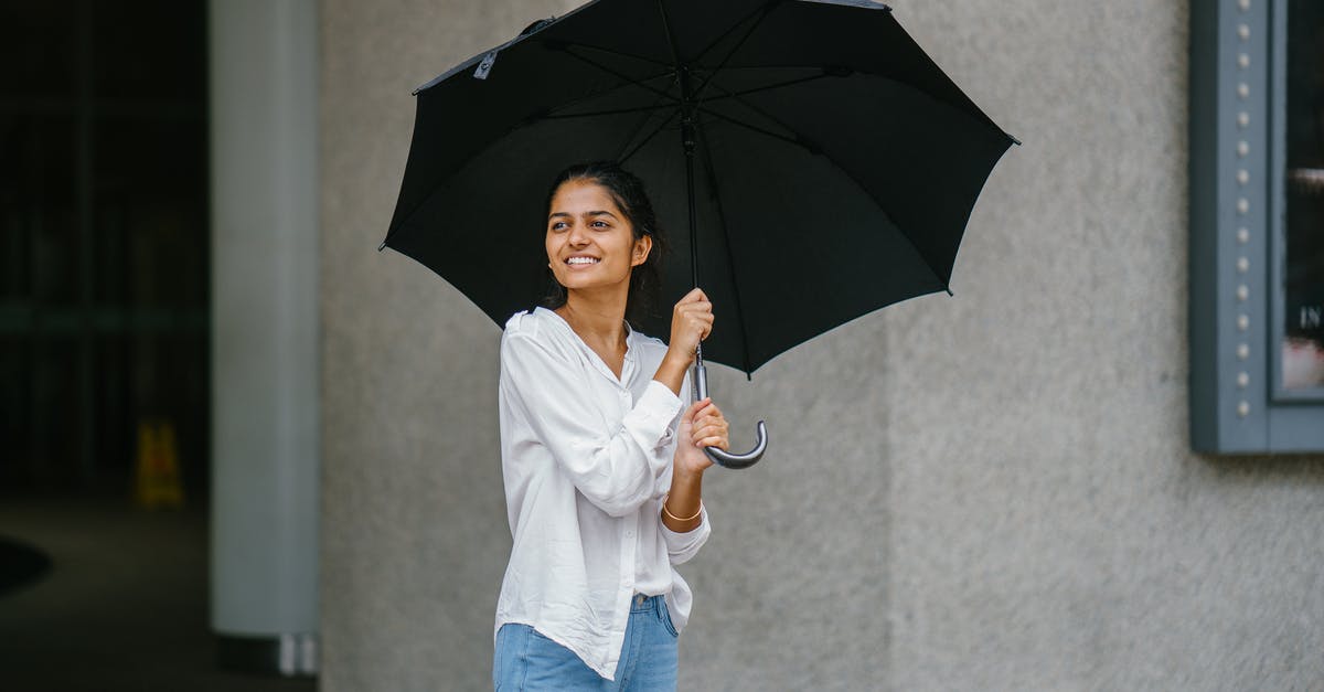 What should I wear in the tropics during the rainy season? - Photo of Woman Wearing White Long-sleeved Shirt and Blue Jeans Holding Black Umbrella