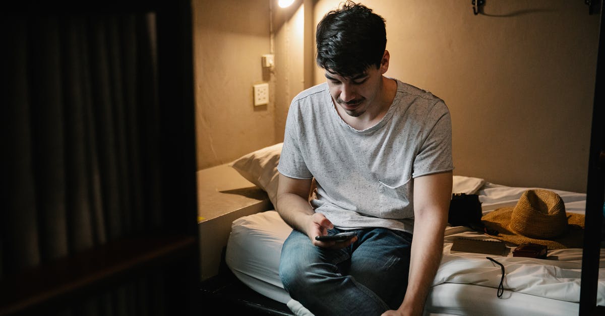 What times do hostels allow you to check in? - Man sitting on bed and using smartphone