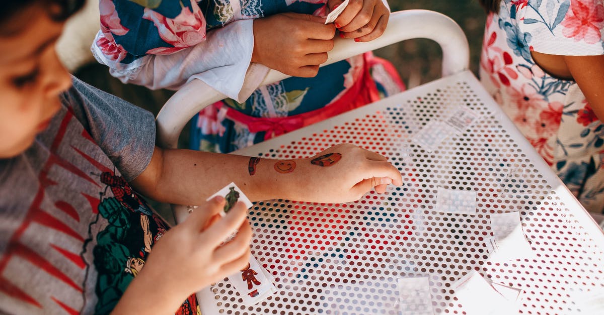 What to do with the small barcode stickers? - From above of anonymous kids in casual clothes standing near white table and playing with small cards in sunny day