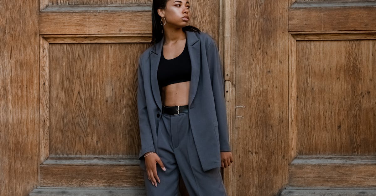 What to wear in Russia - Woman in Black Tank Top and Gray Blazer Standing Beside Brown Wooden Wall