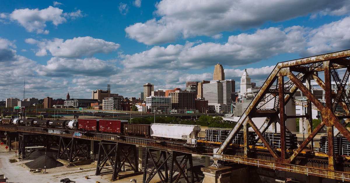 What truly cross-continental train trips still exist? - Freight train crossing railway bridge near industrial buildings against blue sky with clouds on sunny summer day