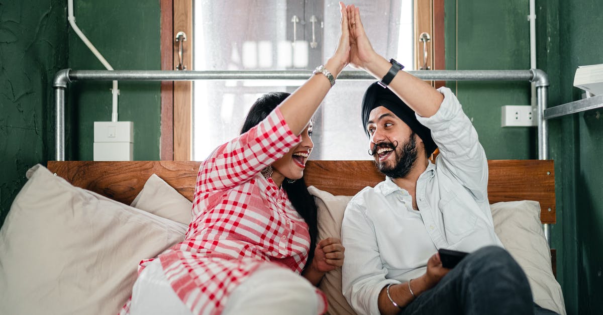 What was the meaning of this Indian gesture/greeting? - Positive adult ethnic couple in casual clothes giving high five to each other while resting on bed in small bedroom with sticking out pipe