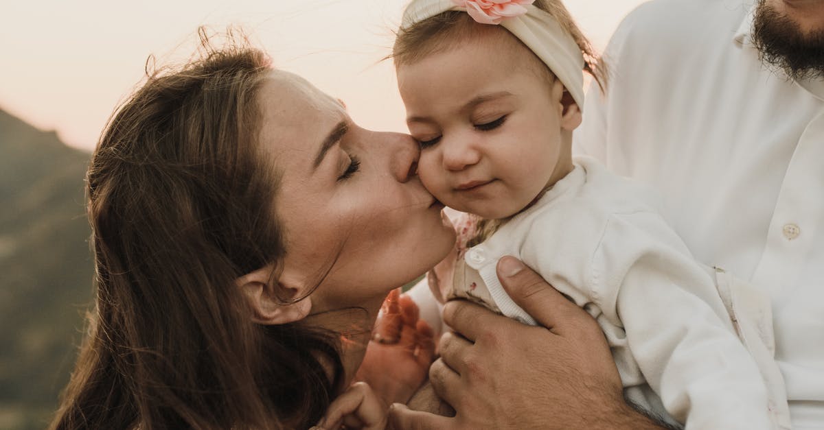 What will happen if a mother with a small child travels in an airplane/airport and the mother will be hospitalized/unable to take care of the child? - Loving mother kissing cute baby daughter held by crop father while having family day in nature
