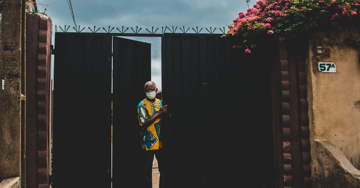 What would be my concourse and gate number for departure? - Anonymous ethnic male in colorful wear and mask standing near gate under cloudy sky during COVID 19 pandemic