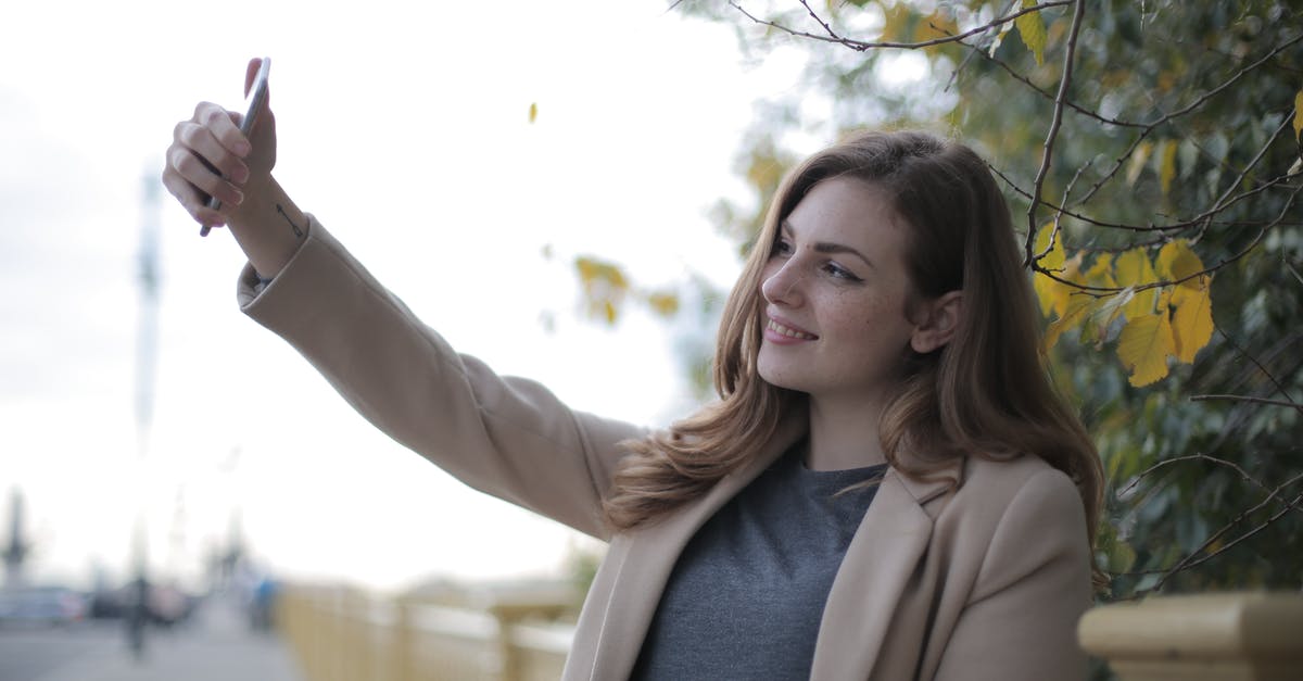 When changing trains when should one use the standalone yellow validitors? - Young woman in coat taking selfie with smartphone on street in overcast weather