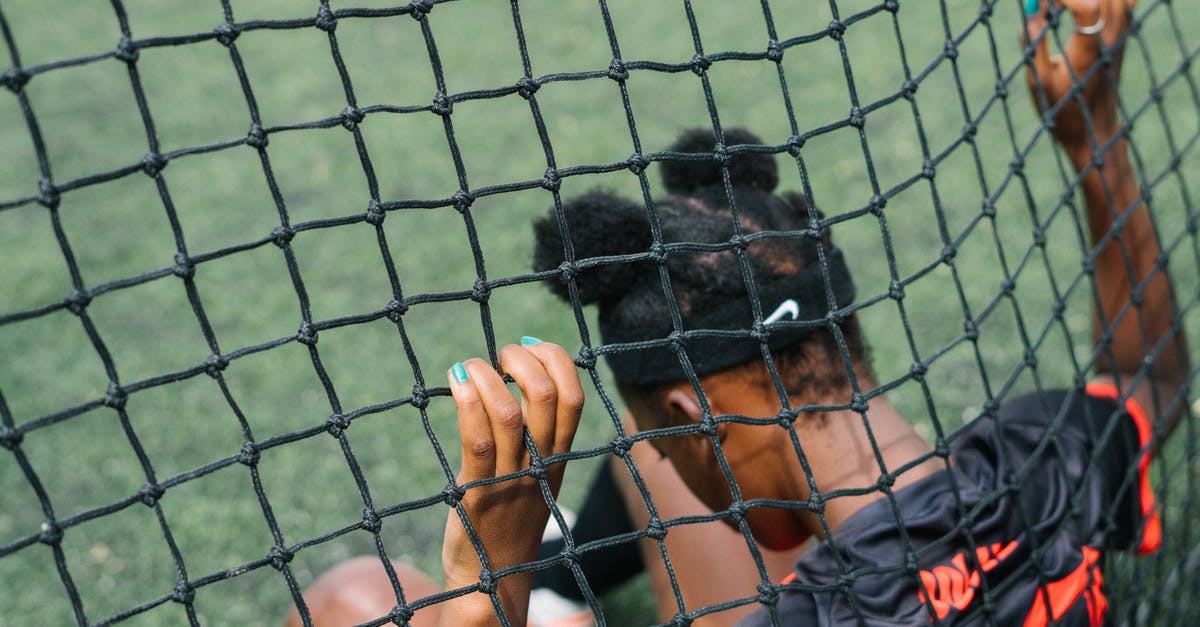 When does an NHL game actually start? - Back view of African American teenage football player sitting on field ground and holding grid of gate while preparing to start play football match