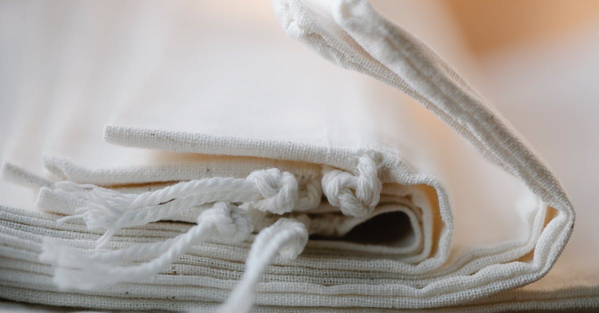 When packing a stack of folded t-shirts in a suitcase, how to reduce the likelihood that they unfold? - Pile of folded white cotton bags with ropes made of ecological cloth placed on table in light room on blurred background