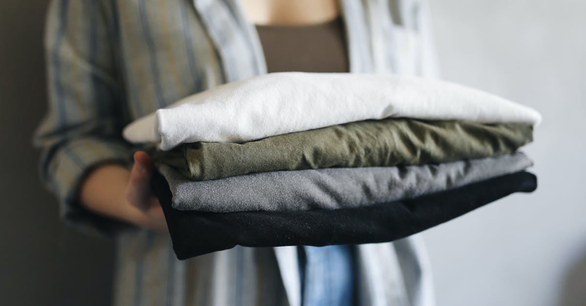 When packing a stack of folded t-shirts in a suitcase, how to reduce the likelihood that they unfold? - Woman in Blue Denim Jeans Holding White Textile