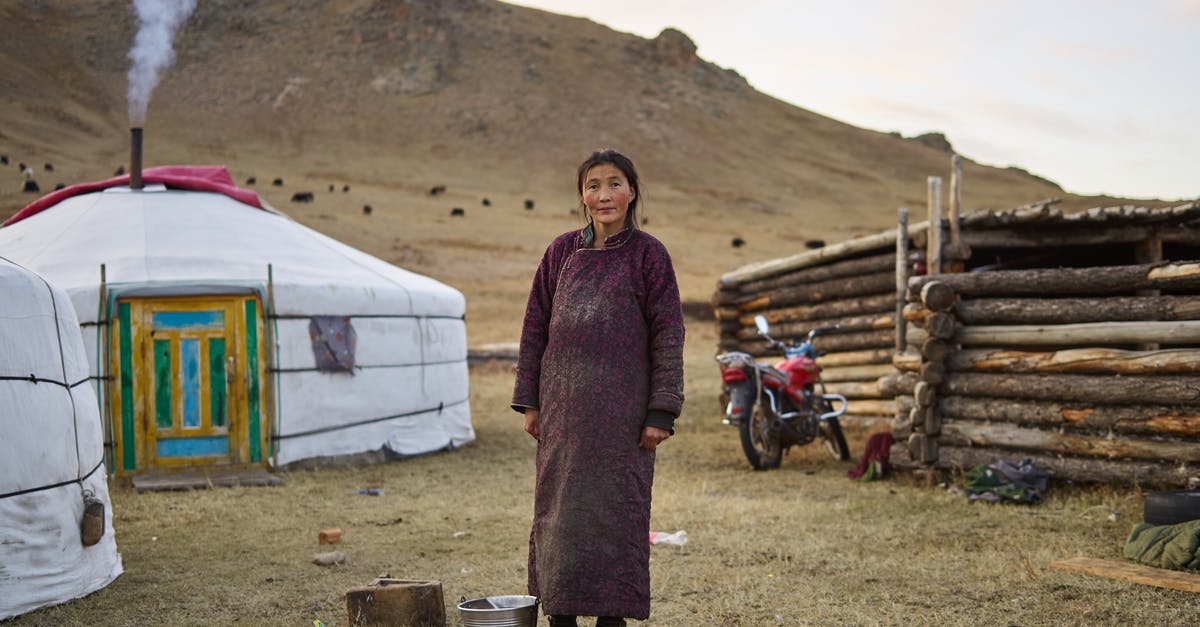 When picking a "luxury hostel" for a business trip, how to ensure it'll be quiet enough? - Full body of middle aged pensive Mongolian female farmer in national clothes looking at camera against yurts in valley
