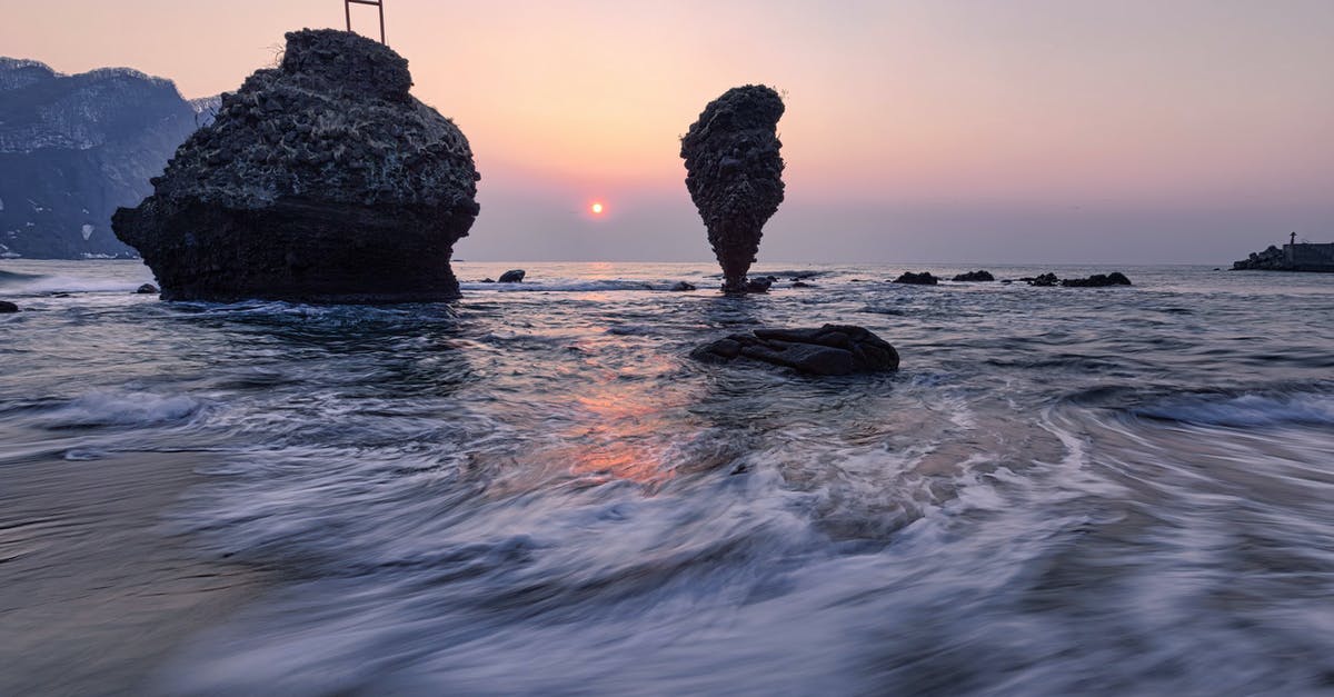 Where's this dale in Sunrise Hill, Alberta? - Long exposure of small vibrant Sun in light blue pink sky over mountain range and cliffs next to coast of endless wavy ocean in evening at dawn