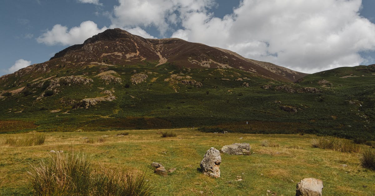 Where's this verdant ridge? - Grassy valley with stones located near green hills against cloudy blue sky in nature