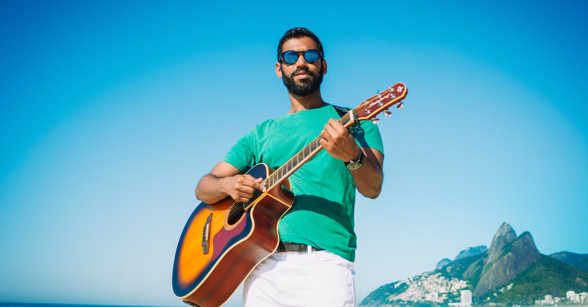 Where can a tourist play horseshoes in Washington, DC? - Low angle of content male in sunglasses playing acoustic guitar while standing on sandy beach near turquoise sea and looking at camera