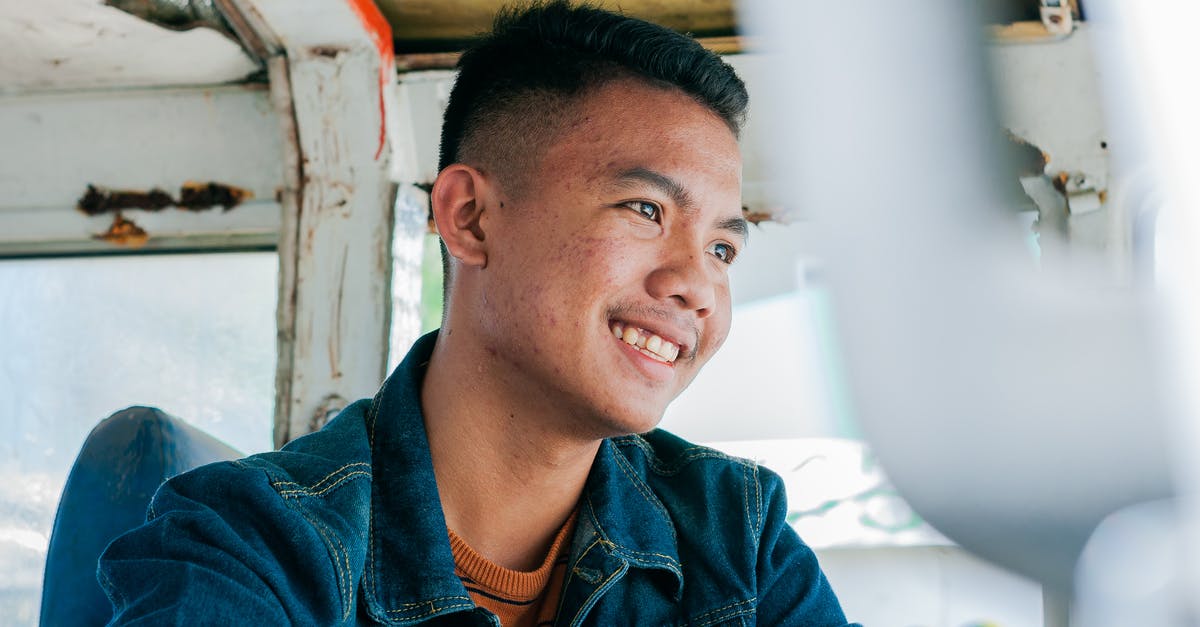 Where can a tourist to Malta ride an articulated bus? - Low angle of cheerful Asian male in denim shirt sitting in weathered public transport smiling away