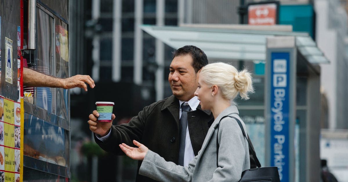 Where can I buy a cup of 'cat poo' coffee (Kopi Luwak) in Melbourne? - Side view of young female manager with ethnic male colleague in formal clothes buying takeaway coffee from booth on city street during break