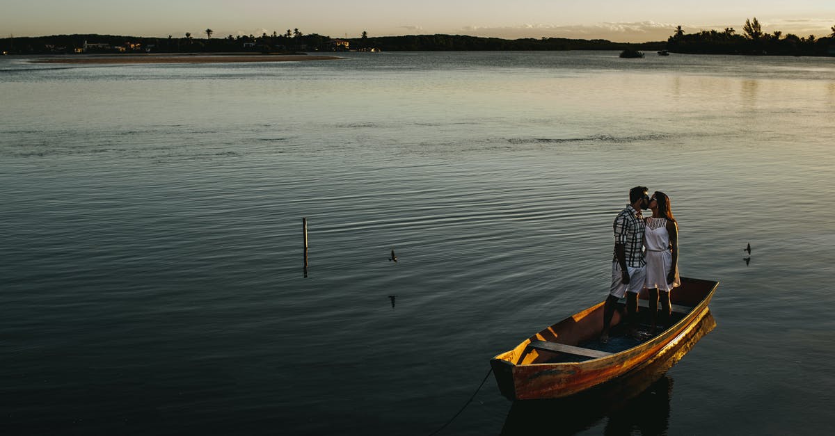 Where can I go by boat from Amsterdam? [closed] - From above of young romantic couple kissing while standing in fishing boat floating on calm lake in evening