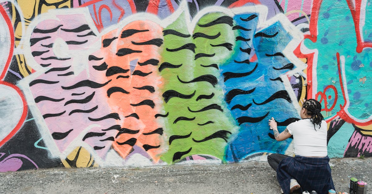 Where can I have a genuine Ainu cultural experience in Hokkaido? - Happy ethnic female artist with braided hair tossing up spray paint can while standing near wall with creative graffiti on street