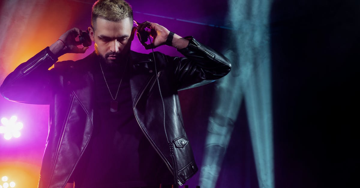 Where can I listen to live “Gypsy” music in Bucharest? - Self assured young bearded male DJ in trendy leather jacket adjusting headphones while performing music on stage in dark illuminated nightclub