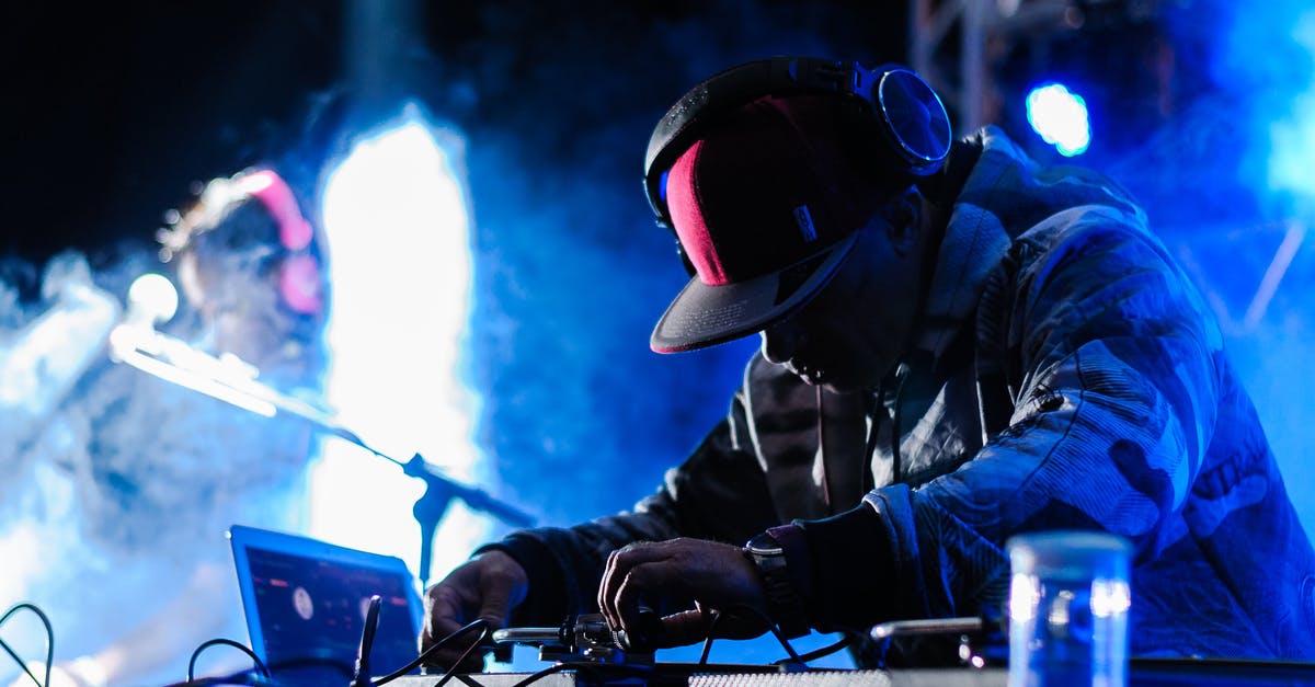 Where can I listen to live “Gypsy” music in Bucharest? - Side view of concentrated African American DJ in headphones performing music at concert in club with neon lights