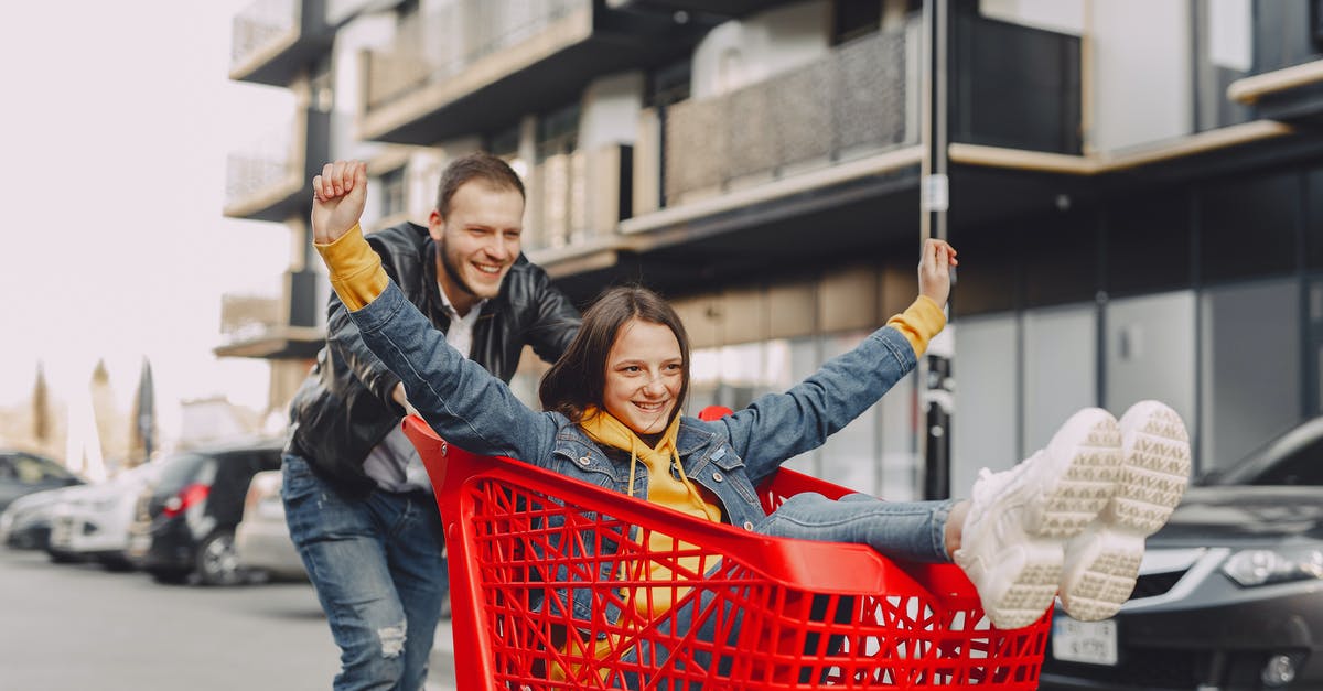 Where can I ride a pump trolley? - Cheerful adult male in casual outfit riding happy girl in jeans clothes on shopping trolley on parking on city street near modern multistory building