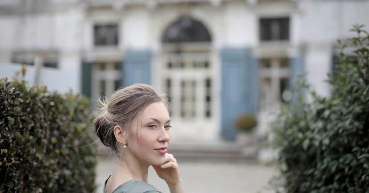 Where can I visit something similar to Kowloon Walled City? - Thoughtful casual lady in gray t shirt with beautiful hairstyle posing and looking away while standing near old building between trimmed bushes of garden