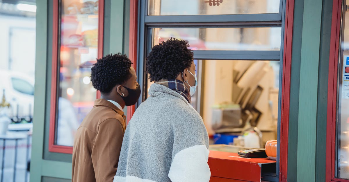 Where can you safely store your belongings in order to travel? [closed] - Side view of African American male in protective masks buying food while standing near window of store on street in city