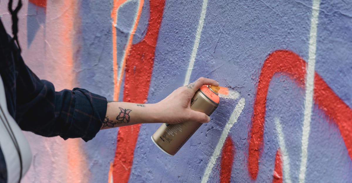 Where in Amsterdam can one legally spray graffiti? - Crop unrecognizable painter with tattoos in black wear spraying orange paint on colorful purple wall with graffiti on street of city