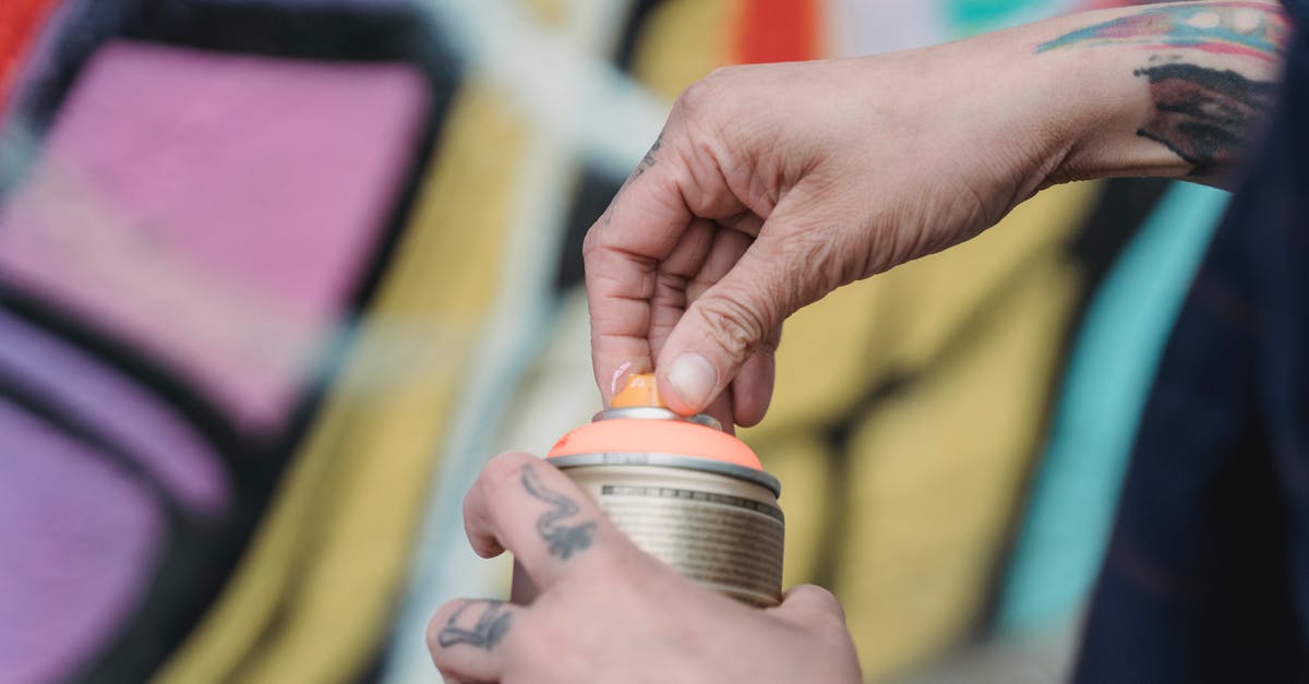 Where in Amsterdam can one legally spray graffiti? - Soft focus of crop unrecognizable painter with tattoos opening spray paint can while standing near colorful wall with creative graffiti